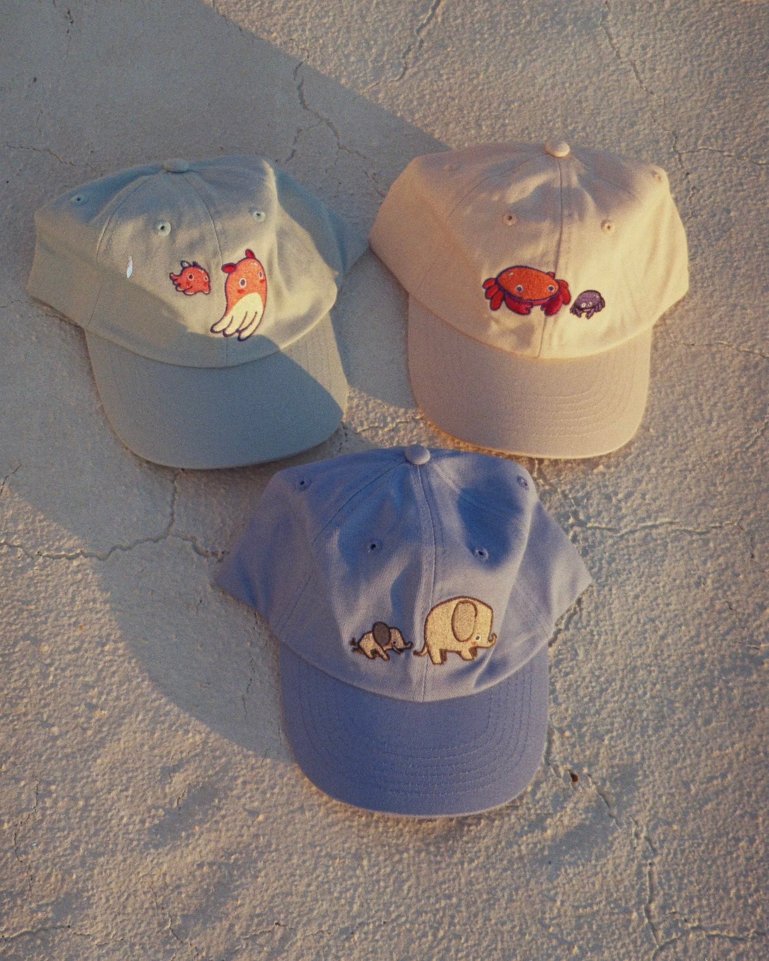 Drei Caps / Mützen für Kinder in hellblaues Cap mit einem rosa Tintenfisch, ein beiges Cap mit zwei Krabben und ein hellblaues Cap mit zwei Elefanten